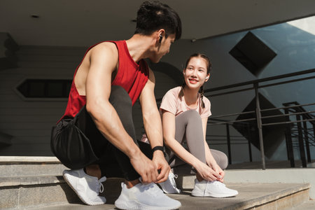 Preparation before jogging exercise. Together young Asian man and woman tying shoelace on her running shoes. Fitness and sport activity. Healthy exercise concept.の写真素材
