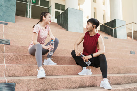 Young Asian couple athlete drinking water after exercising outdoors in park. Drinking water from bottle, Healthy exercise concept.の写真素材