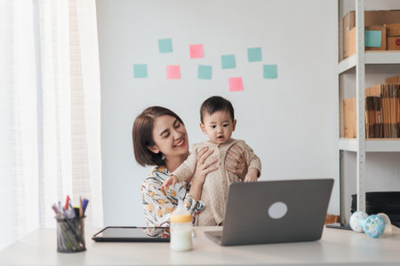 A boy Asian baby in mother's arms, and use computer laptop with video calls with father or long-distance relatives. Tech-Fueled Family Love Concept.の写真素材