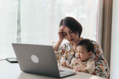 Asian mother are stressed work from home and raising their children. A little boy Asian baby is disturbing his mother while she is working at home. Concept problem of working from home.の写真素材