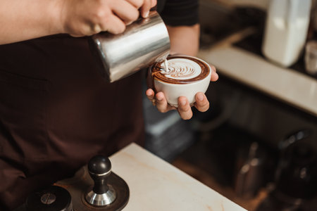 Barista pouring milk foam to making latte art coffee. Young man barista working at coffee shop. Latte art menu coffee, Espresso, Coffee menu making concept. Selective focus.の写真素材