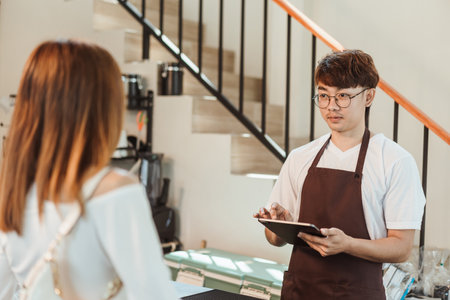 Asian man waitress use digital tablet take order service female customer at coffee shop. SME business coffee shop concept.の写真素材
