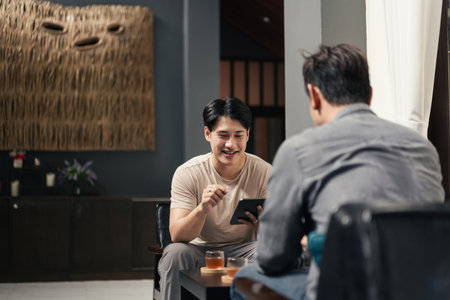 Smiling young Asian man friend talking and sharing massage experience in spa salon. Two Asian people talking in lobby.の写真素材