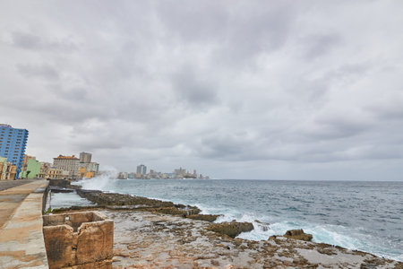 Sea waves breaking on a stone wall on the shore with buildings in the background on the Malecon in Cubaの写真素材