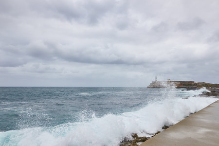 Sea waves breaking on a stone wall on the shore with buildings in the background on the Malecon in Cubaの写真素材