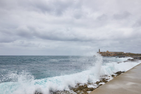 Sea waves breaking on a stone wall on the shore with buildings in the background on the Malecon in Cubaの写真素材