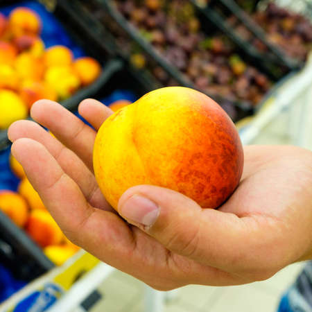 man holding a peach in a shopping center next to the counterの写真素材