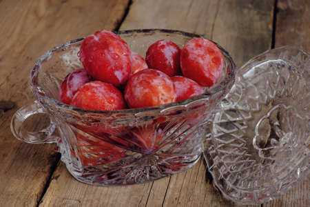 bright fresh plums in a crystal bowl on the old wooden boardsの写真素材