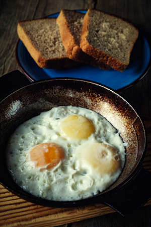 fried eggs in an old pan on wooden boards and near all the bread in retro styleの写真素材