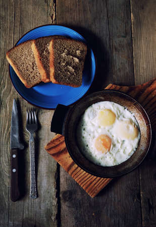 fried eggs in an old pan on wooden boards and near all the bread in retro styleの写真素材