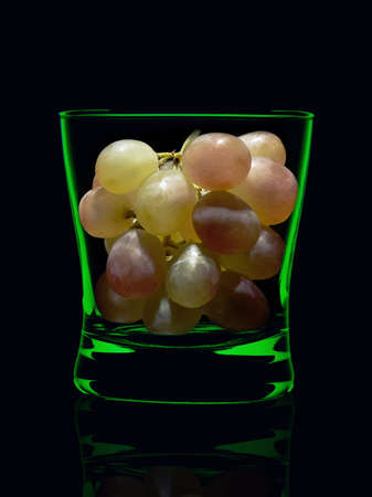 Promotional shot of grapes in a glass of whiskey with green rendered on black background.の写真素材