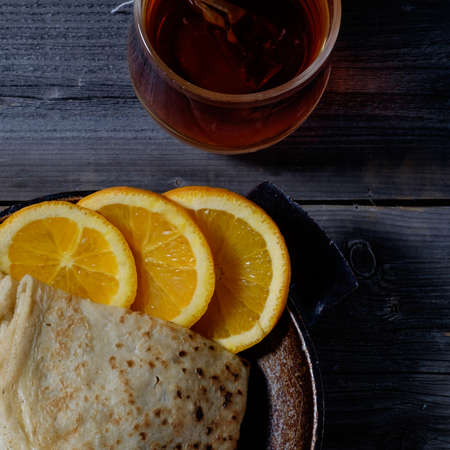 Orange with pancakes on wooden boards, covered with red cellar mysterious light.