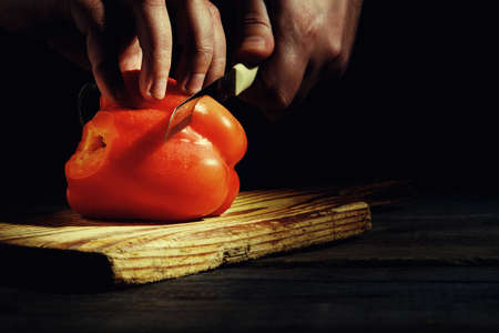 Man cuts tasty red peppers on a table made of planks, a beautiful lit basement light.の写真素材