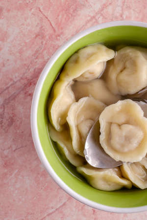 Fresh homemade ravioli in a green plate on a pink stone, illuminated by soft light from the window.の写真素材