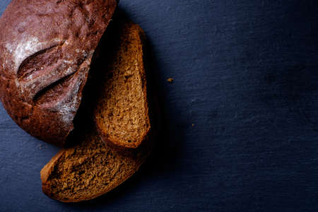 Delicious, fresh black bread on a black board in the studio.の写真素材