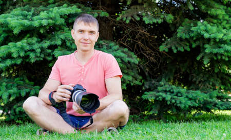 A guy in a pink shirt with a camera on the background of beautiful nature.の写真素材