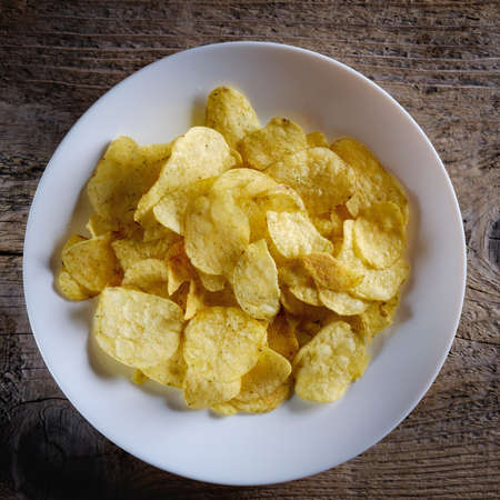 Chips in a white plate on a wooden background.