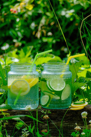 Lemonade in glass jars with tubes for cocktail on the blackboard in garden, on green blurred backgroundの写真素材