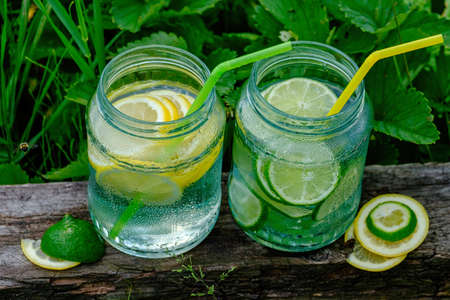 Lemonade in glass jars with tubes for cocktail on the blackboard in garden, on green blurred...