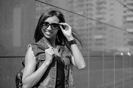 Beautiful sexy young brunette woman with long wavy hair thin slim figure perfect body and beautiful face make-up, wearing a black suit and vintage denim jacket. summer accessory, black backpackの写真素材