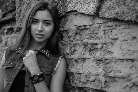 Beautiful sexy young brunette woman with long wavy hair thin slim figure perfect body and beautiful face make-up, wearing a black suit and vintage denim jacket. summer accessory, black backpackの写真素材