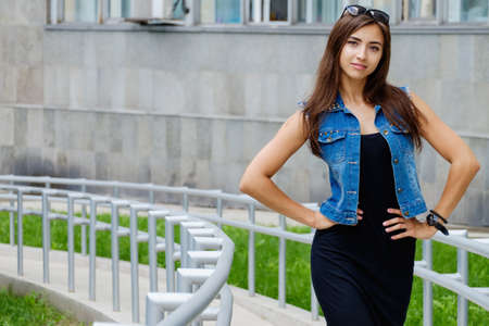 Beautiful sexy young brunette woman with long wavy hair thin slim figure perfect body and beautiful face make-up, wearing a black suit and vintage denim jacket. summer accessory, black backpackの写真素材