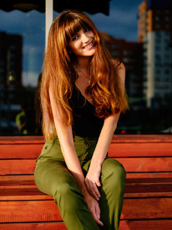 Beautiful red-haired young woman, pants, black top and bags walking on the streetの写真素材