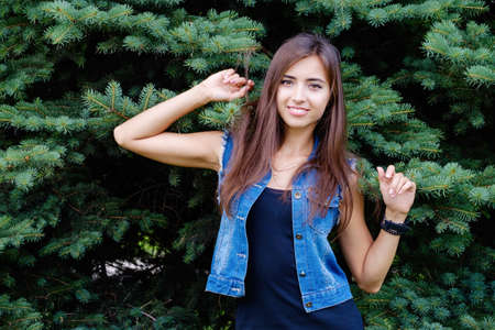 Beautiful sexy young brunette woman with long wavy hair thin slim figure perfect body and beautiful face make-up, wearing a black suit and vintage denim jacket. summer accessory, black backpackの写真素材