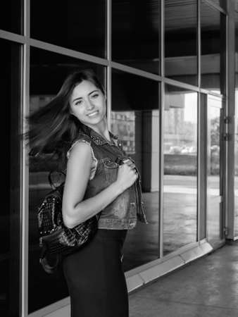 Beautiful sexy young brunette woman with long wavy hair thin slim figure perfect body and beautiful face make-up, wearing a black suit and vintage denim jacket. summer accessory, black backpackの写真素材