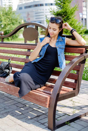 Beautiful sexy young brunette woman with long wavy hair thin slim figure perfect body and beautiful face make-up, wearing a black suit and vintage denim jacket. summer accessory, black backpackの写真素材