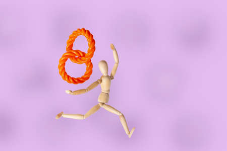 Wooden mannequin running with a rope in the shape of a number eight on a purple backgroundの写真素材
