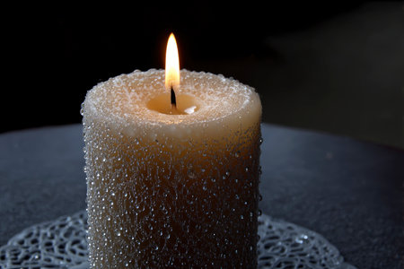 Burning candle with drops of water on a black background close upの素材