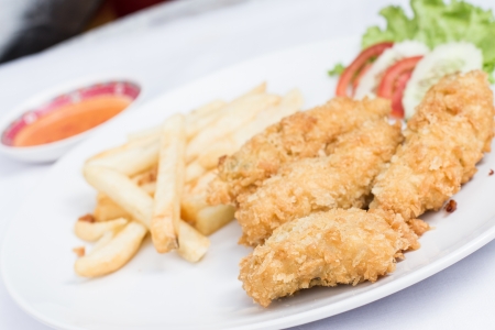 Closeup of deep fried Fish and chips with and vegetables home made on white dishの写真素材