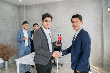 Manager checking hand and giving employee the trophy award for success in business while another...