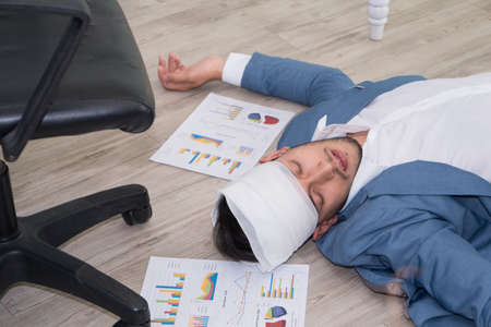 Sick businessman sleeping on floor while using laptop to work hard at office