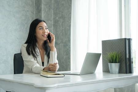 Asian businesswoman working on laptop and phone in her workstation.