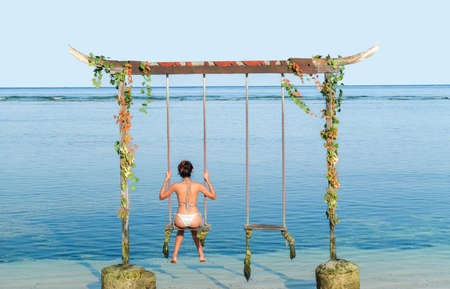 Woman relaxing in the swing in the paradise turquoise sea, Gili Trawangan island, Indonesiaの写真素材