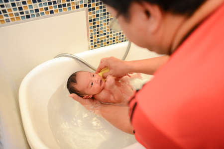 Newborn baby boy having bath in tubby on Father's hand. Newborn Baby's First Bathの写真素材