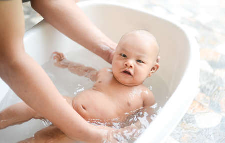 4 month old Asian baby boy having bath in tubby on Father's hand.の写真素材