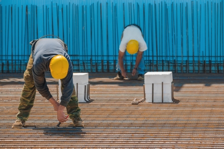 Authentic construction workers installing binding wires to reinforcement steel bars in front of a blue insulated surface prior to pouring concreteの写真素材