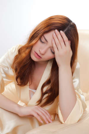 nice girl in beige home dressing gown with headacheの写真素材
