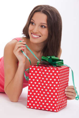 What surprise Surprised young womanin a red vest and blue jeans opening gift box and smiling while standing on white backgroundの写真素材