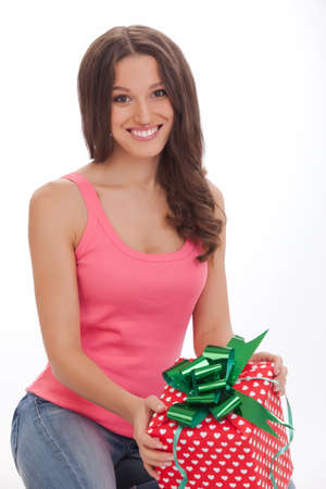 What surprise Surprised young womanin a red vest and blue jeans opening gift box and smiling while standing on white backgroundの写真素材