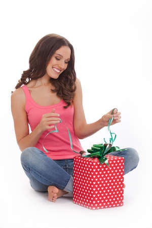What surprise. Surprised young woman in a red t-shirt and blue jeans s opening gift box and smiling while standing on white backgroundの写真素材