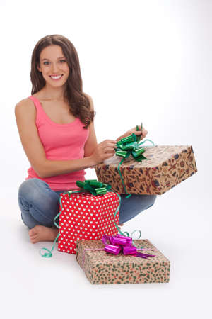 What surprise Surprised young womanin a red vest and blue jeans opening gift box and smiling while standing on white backgroundの写真素材