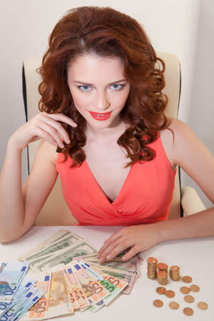 young girl at table with greedy countsmoney lying on table and looking at  cameraの写真素材