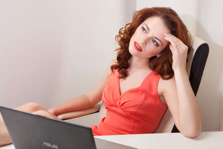 beautiful girl in  pink dress sitting in  office chair behind a white Desk with his feet on  tableの写真素材