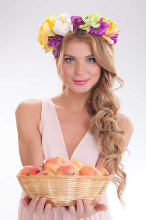 beautiful girl with long blond hair in beige dress with a wreath of flowers on her head and a basket of applesの写真素材
