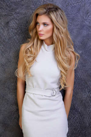 beautiful woman with long hair in beige dress next to the dark wallの写真素材