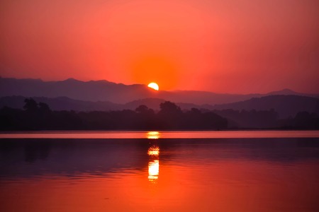 HALF SUN RISE BEHIND THE MOUNTAINS AND REFLECTION OF SUN ON WATERの写真素材